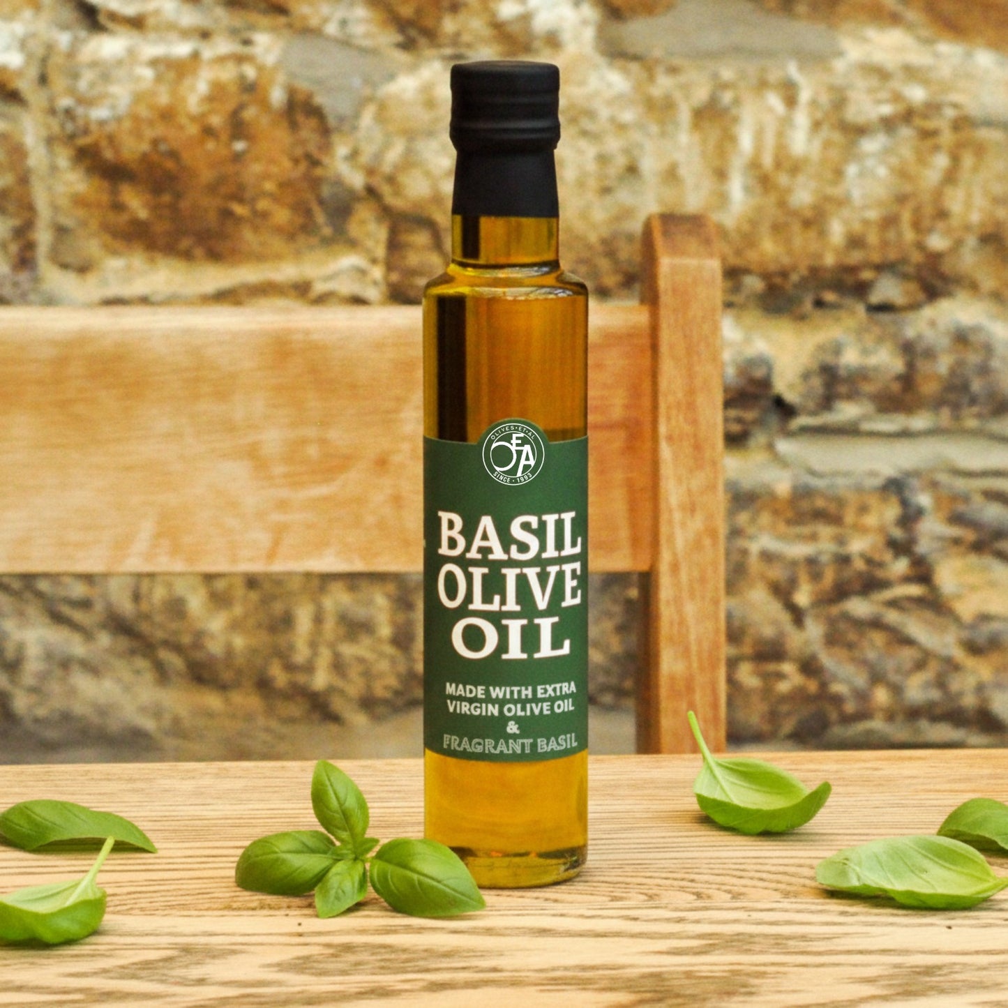 Bottle of basil olive oil with basil leaves on a wooden surface and stone background