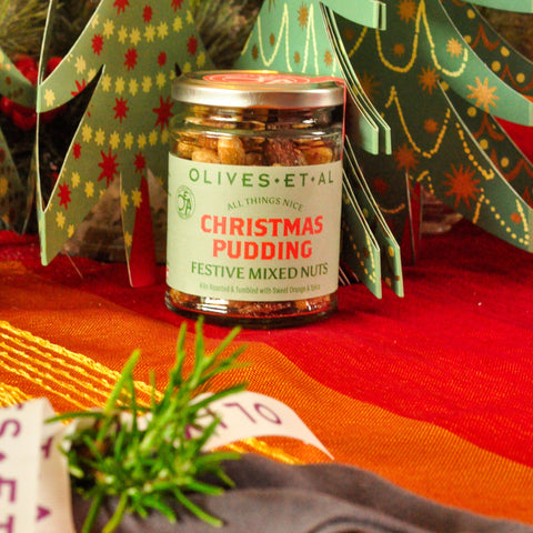 Jar of Christmas pudding nuts with decorative paper trees on a festive table setting.
