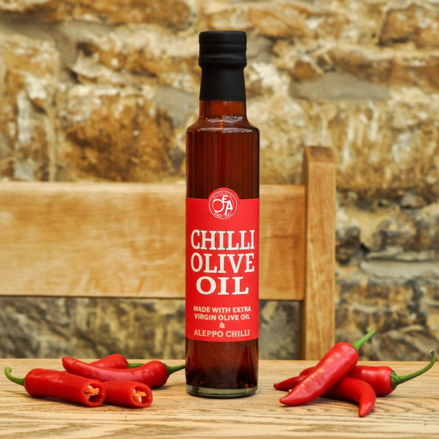 Bottle of Chilli Olive Oil with red label on a wooden surface with red chili peppers.