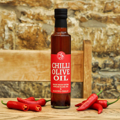 Bottle of Chilli Olive Oil with red label on a wooden surface with red chili peppers.