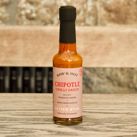 Bottle of Raw & Hot Chipotle Chilli Sauce on a wooden surface with a blurred background