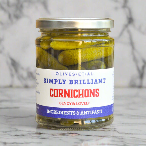 A glass jar filled with pickled cornichons in brine on a marble worktop