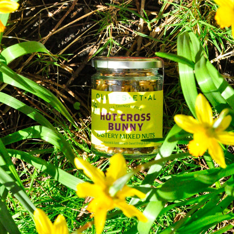 Jar of 'Hot Cross Bunny' kiln roasted nuts surrounded by yellow flowers and green grass