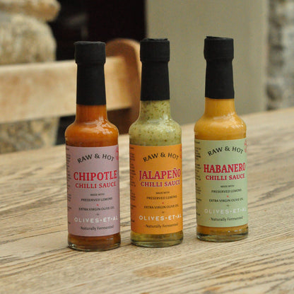 Three bottles of Raw & Hot chili sauces on a wooden surface.