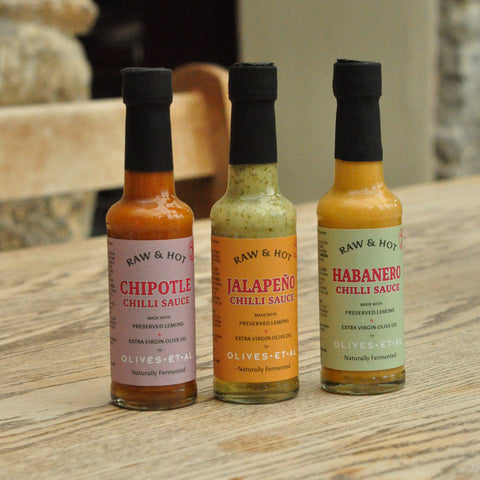 Three bottles of Raw & Hot chili sauces on a wooden surface.
