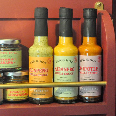 Three bottles of Raw & Hot chilli sauces on a shelf with a red background