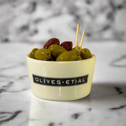 A ceramic bowl containing pitted green and Kalamata olives with fennel and orange, branded with 'OLIVES.ET.