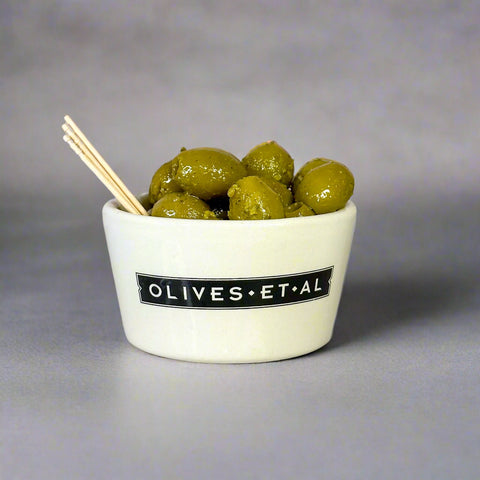 Bowl of olives with a label 'Olives Et Al' on a marble surface.