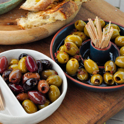 Assorted olives in bowls with bread on a wooden surface