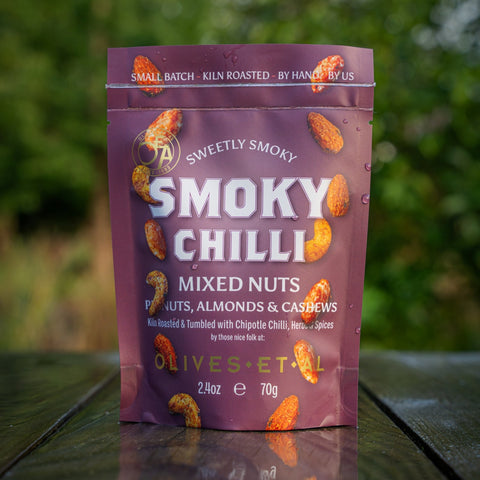 Purple package of smoky chilli mixed nuts on a wooden surface with a blurred green background