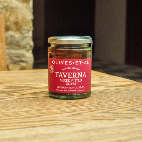 Jar of Taverna olives on a wooden surface with a stone wall background