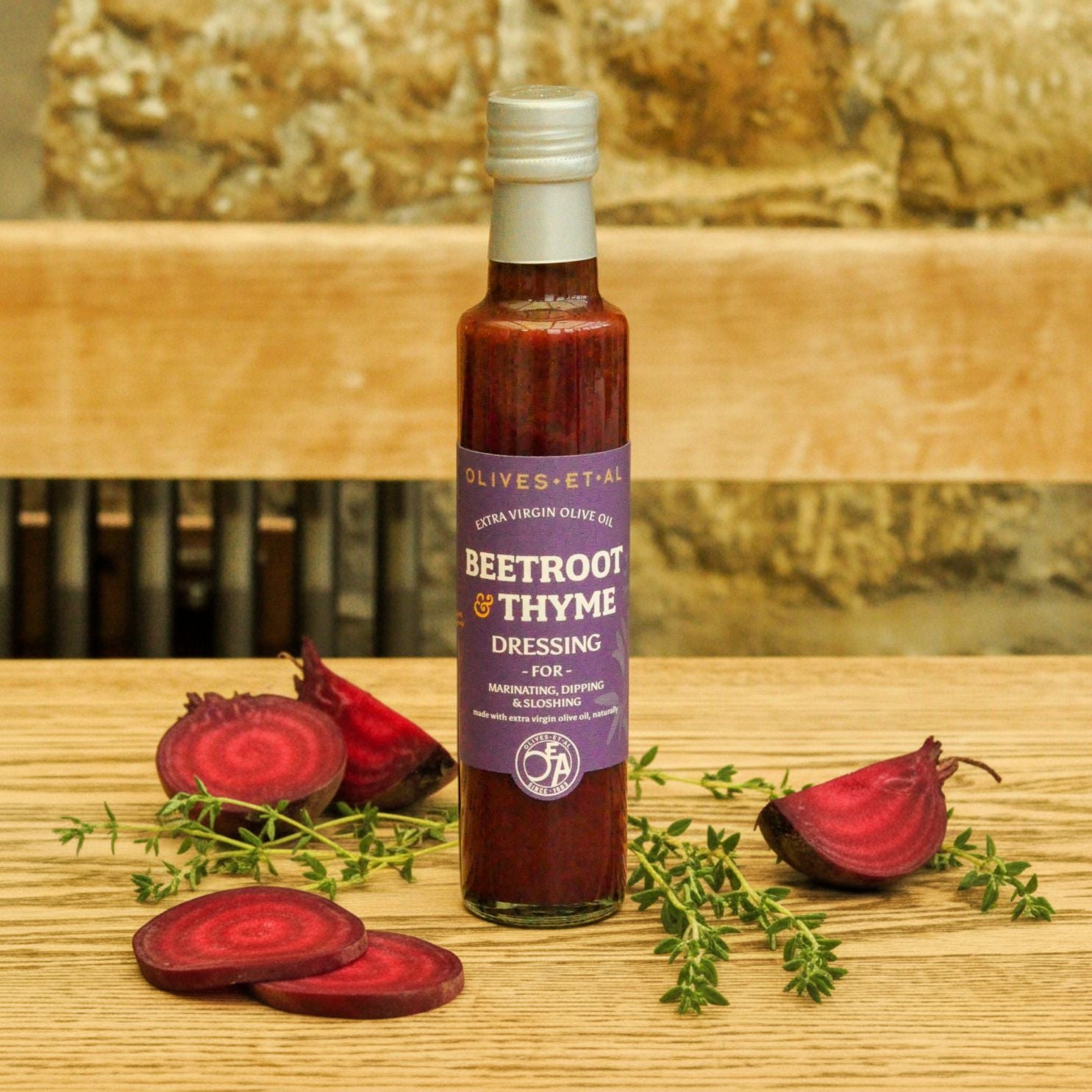 Bottle of Beetroot & Thyme dressing on a wooden surface with beetroot and thyme leaves.