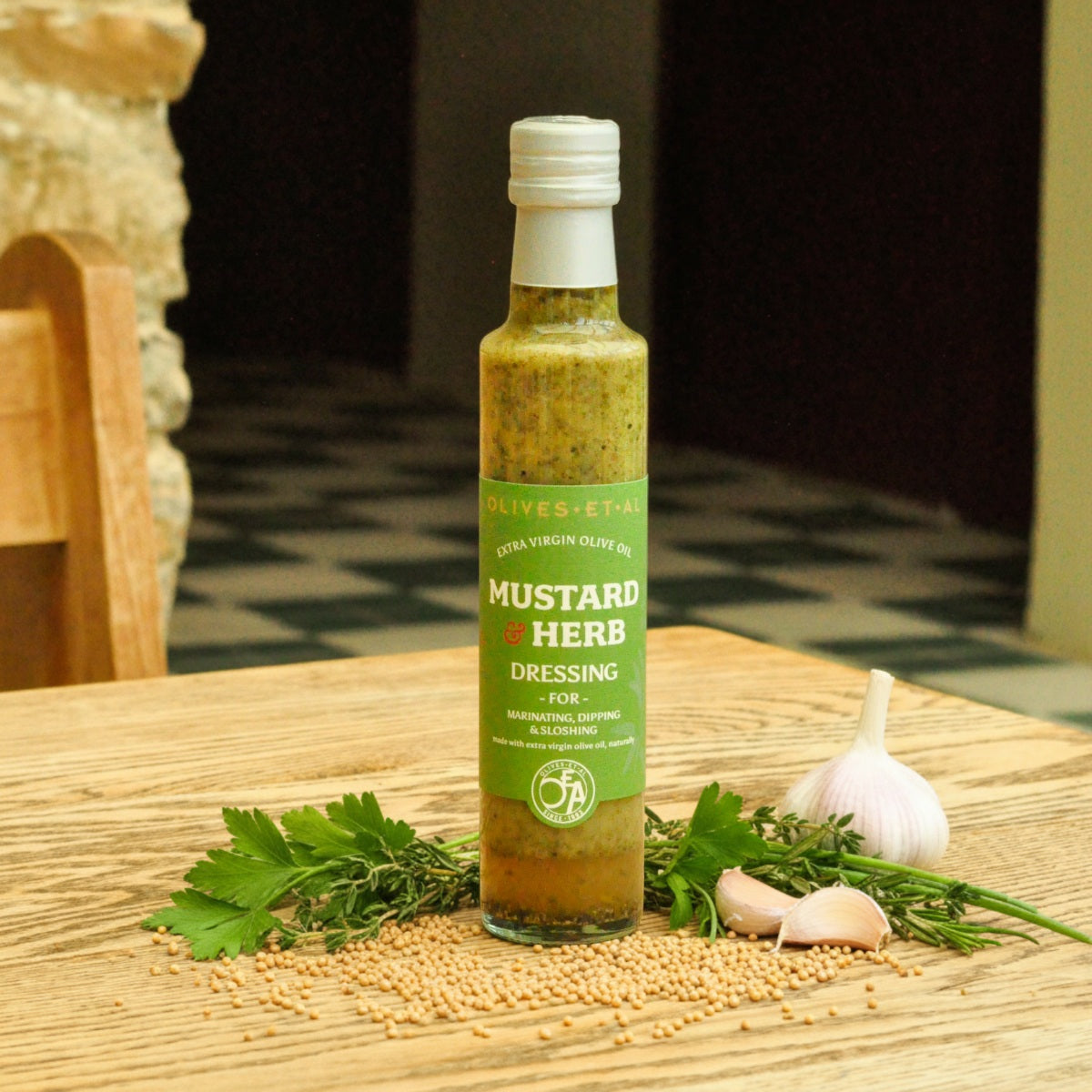 Bottle of mustard herb dressing on a wooden table with herbs and garlic.