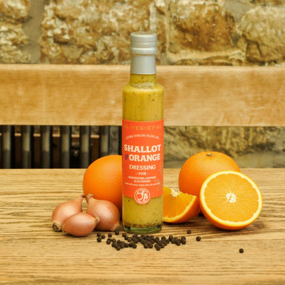 Bottle of 'Shallot Orange Dressing' with oranges and shallots on a wooden surface.