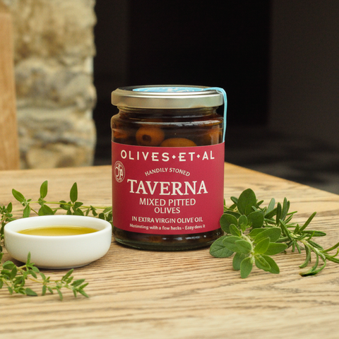 Jar of Olives et al Taverna olives on a wooden surface with herbs and olive oil.